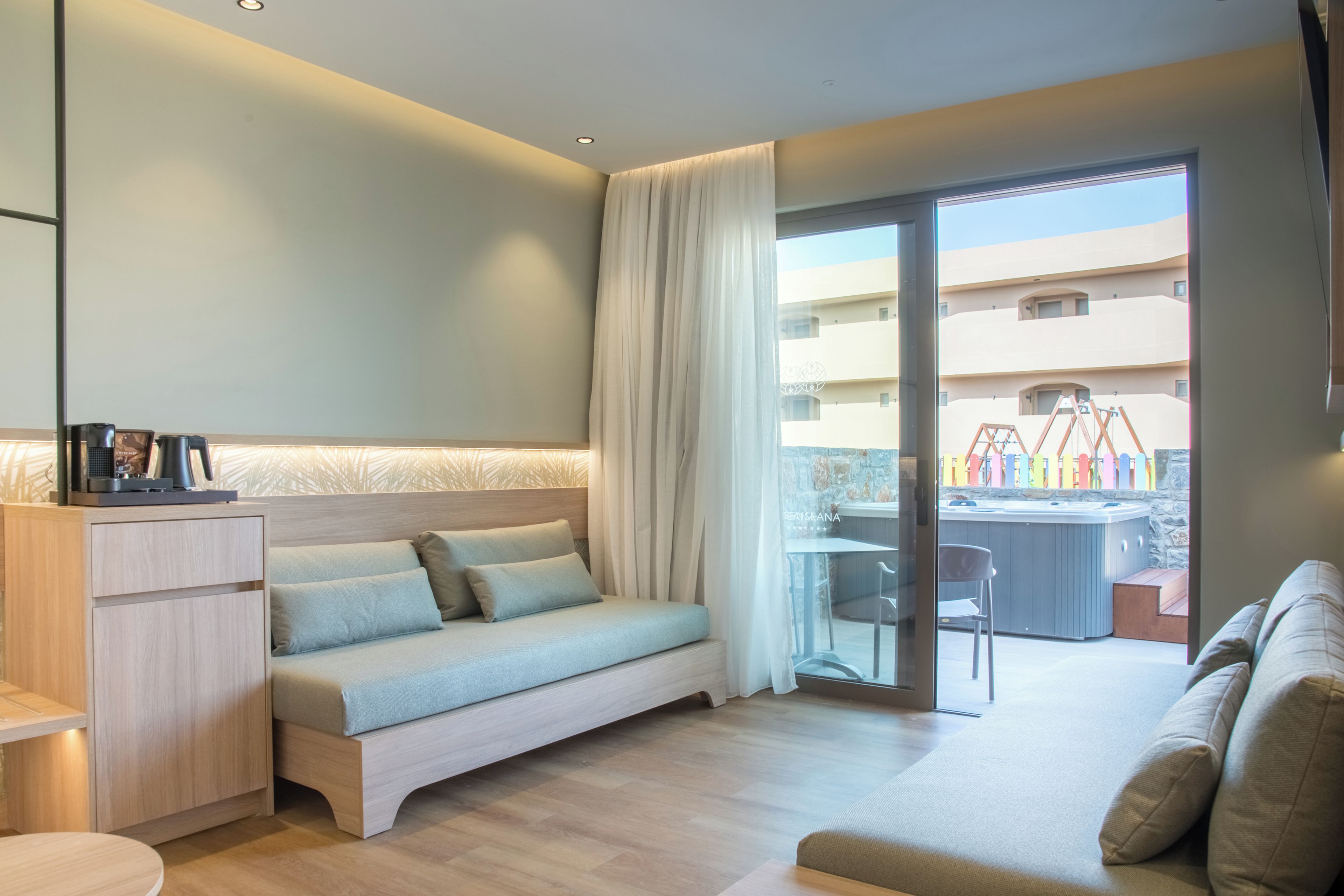 A modern hotel room with a sofa, a small table, and a view of the outdoor area.