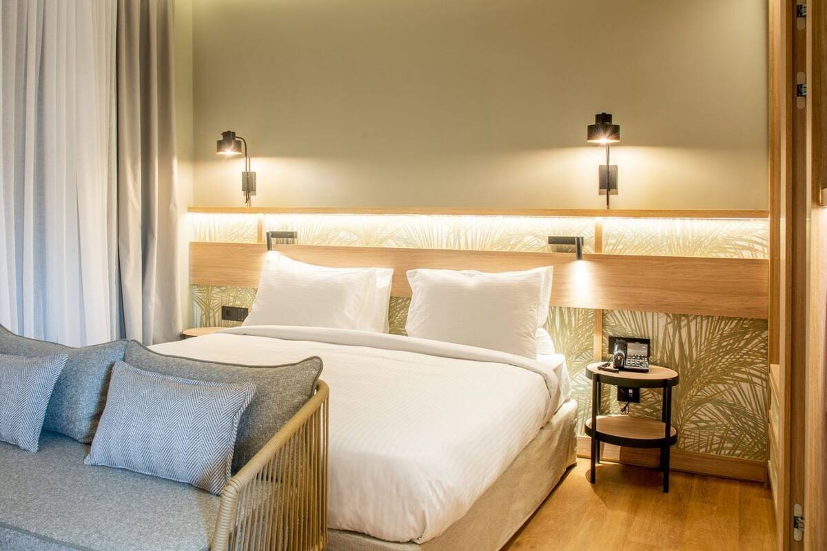 A hotel room with a bed, two bedside tables with lamps, a sofa with cushions, and a curtain.