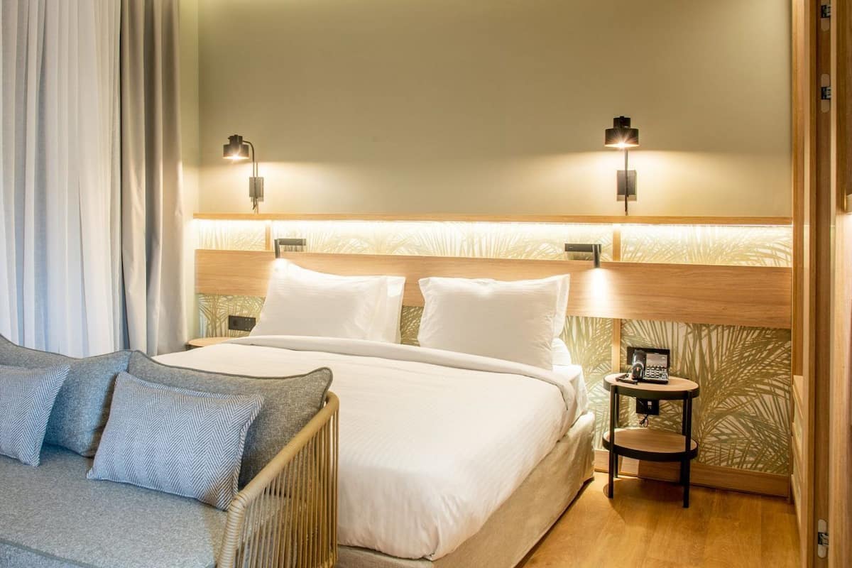 A hotel room with a bed, two bedside tables with lamps, a sofa with cushions, and a curtain.