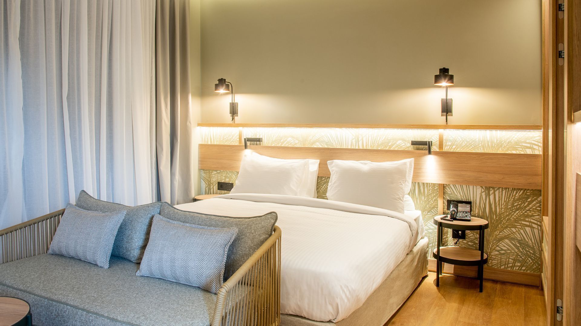 A hotel room with a large bed, two bedside tables, a small sofa, and a curtain.