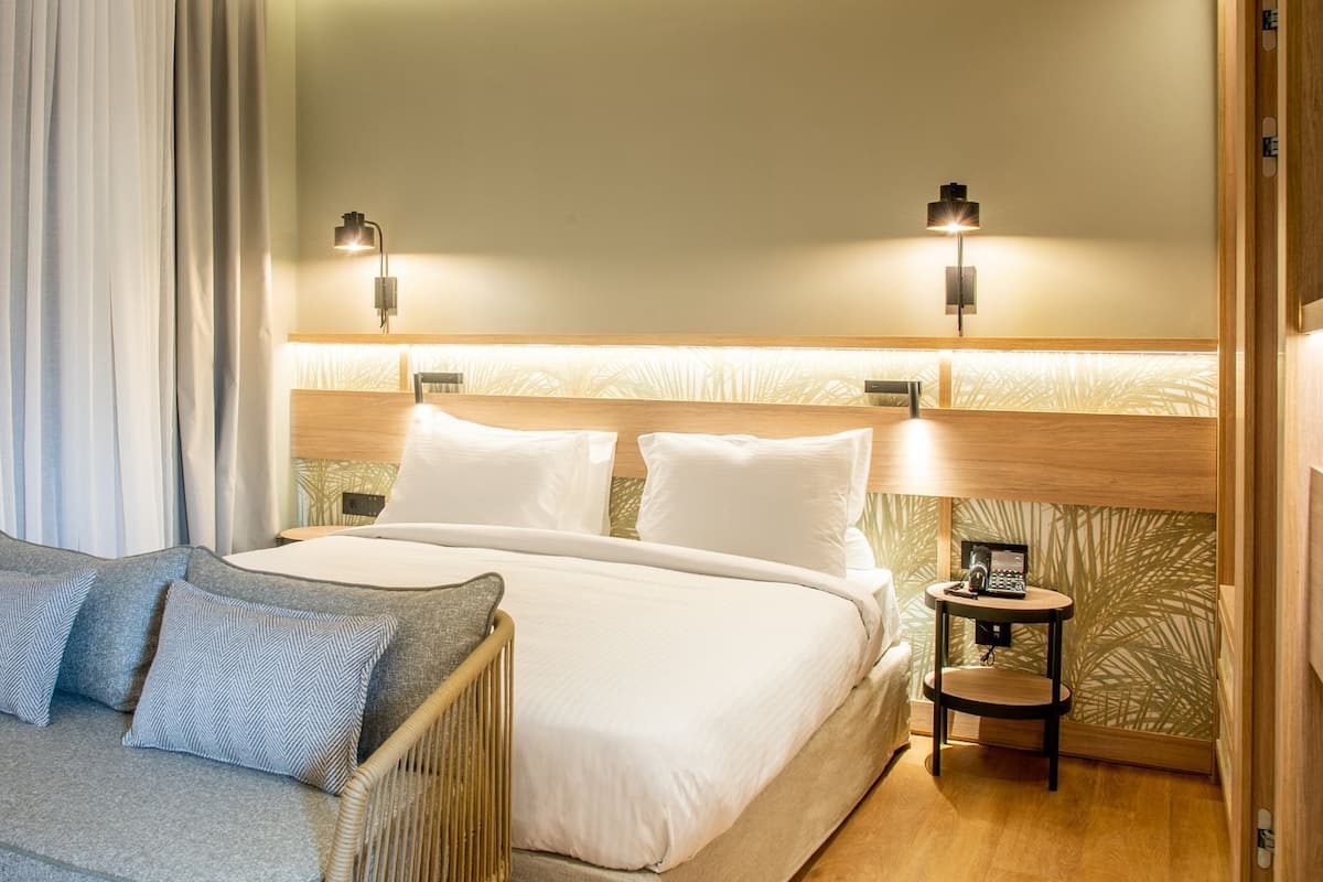 A hotel room with a large bed, two bedside tables, a small sofa, and a curtain.
