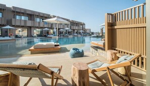 A poolside area with lounge chairs, a wooden deck, and a view of a building in the background. - Senseana Seaside Resort And Aquadventure (Analipsis)
