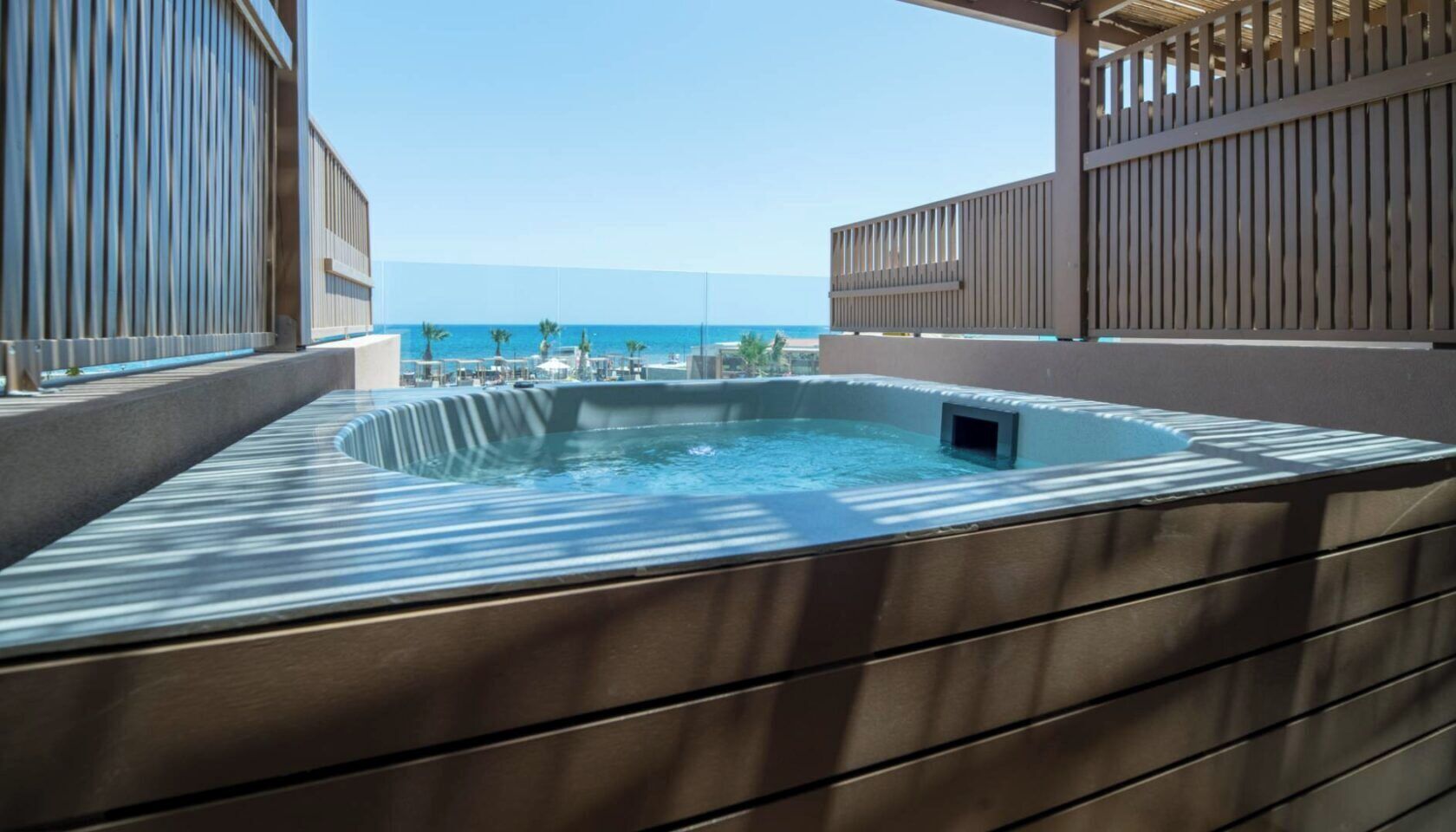 A hot tub with a view of the ocean, surrounded by a wooden deck and a metal railing.