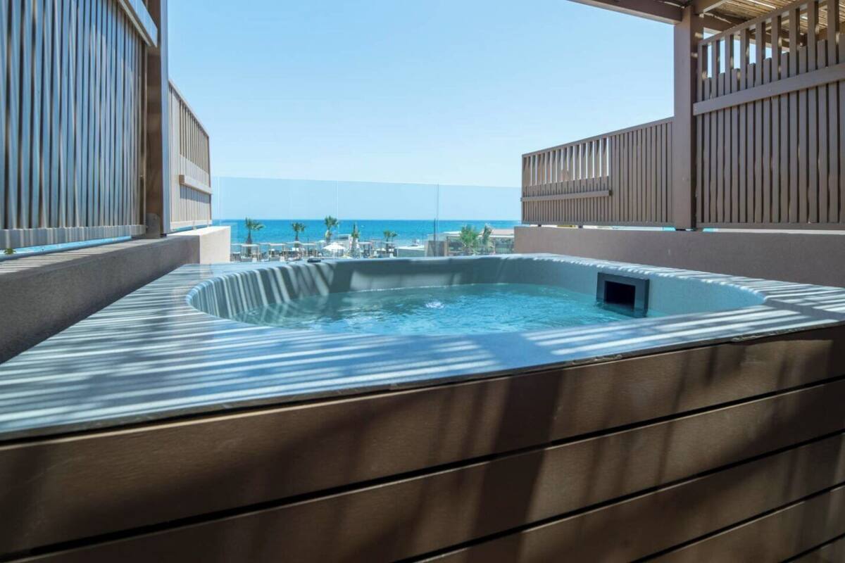 A hot tub with a view of the ocean, surrounded by a wooden deck and a metal railing.