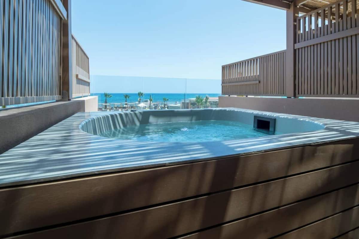 A hot tub with a view of the ocean, surrounded by a wooden deck and a metal railing.