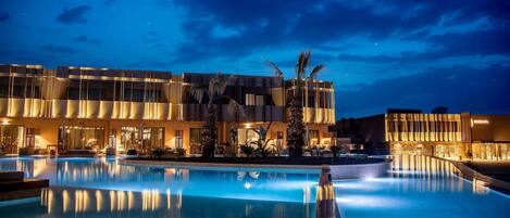 A hotel with a large swimming pool, palm trees, and modern architecture.