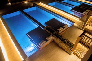 A series of rectangular pools with steps leading into them, surrounded by stone walls and wooden benches. - Senseana Seaside Resort And Aquadventure (Analipsis)