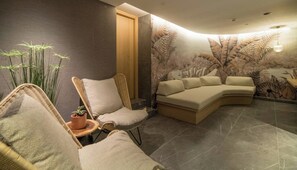 A modern lounge area with a curved sofa, a wicker chair, and a small table with a plant. - Senseana Seaside Resort And Aquadventure (Analipsis)