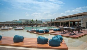 A pool area with lounge chairs and tables, surrounded by buildings. - Senseana Seaside Resort And Aquadventure (Analipsis)