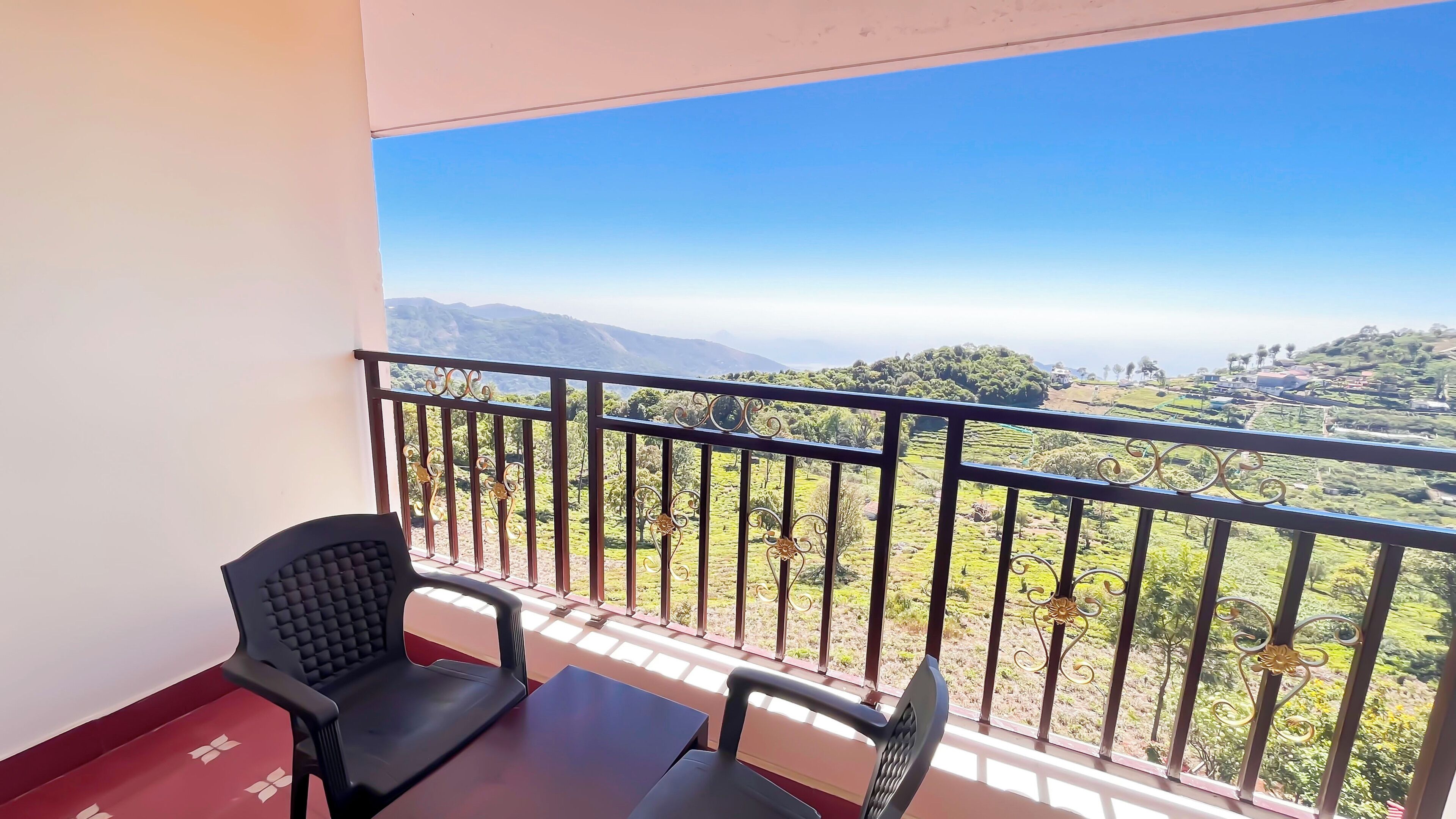 A balcony with a table and two chairs, overlooking a green landscape with hills and trees.