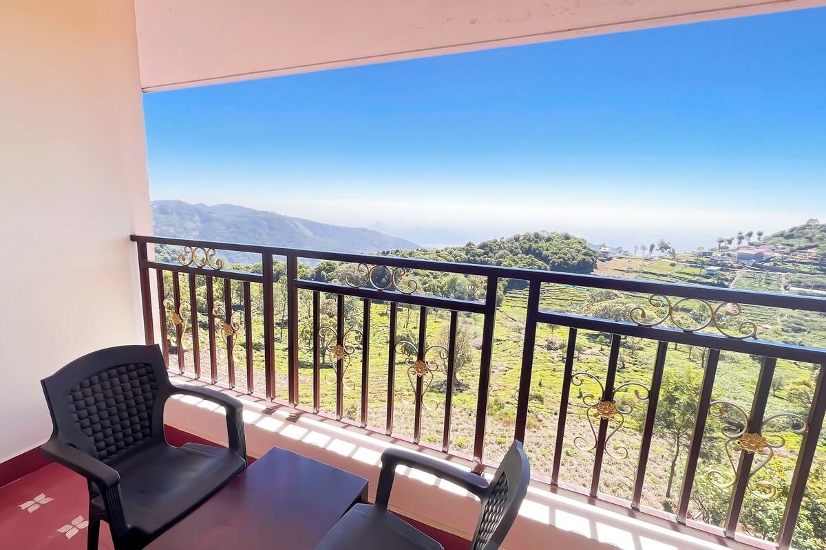 A balcony with a table and two chairs, overlooking a green landscape with hills and trees.