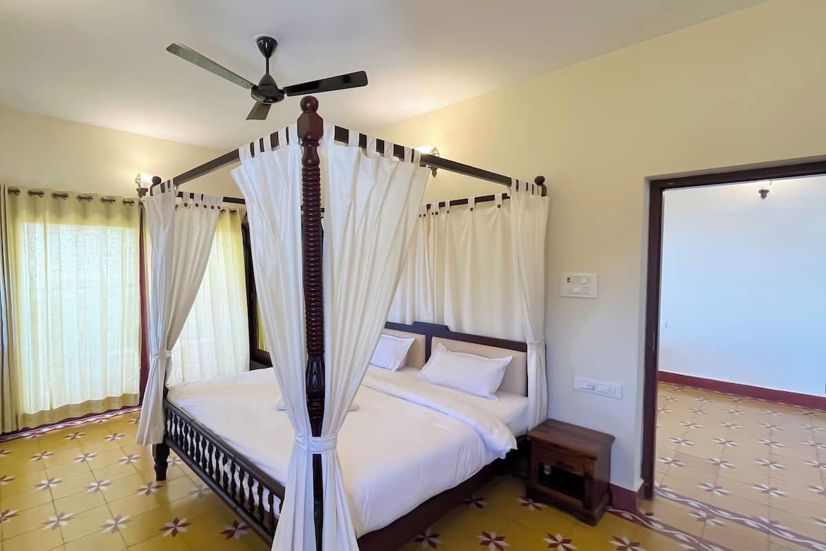 A four-poster canopy bed with white bedding, a ceiling fan, and a tiled floor.