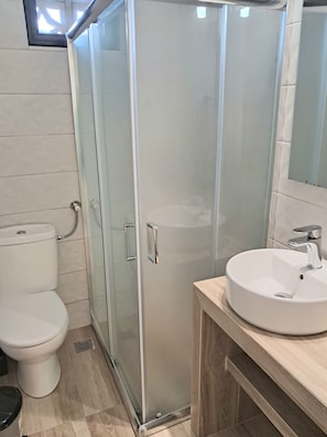 Uma casa de banho moderna com cabine de duche em vidro, sanita branca e lavatório redondo com espelho em cima.