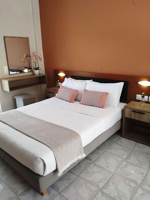 A neatly made bed with a white comforter and pink pillows, a bedside table with a lamp, and a wall-mounted mirror. - Asteri Studios (Zakynthos)