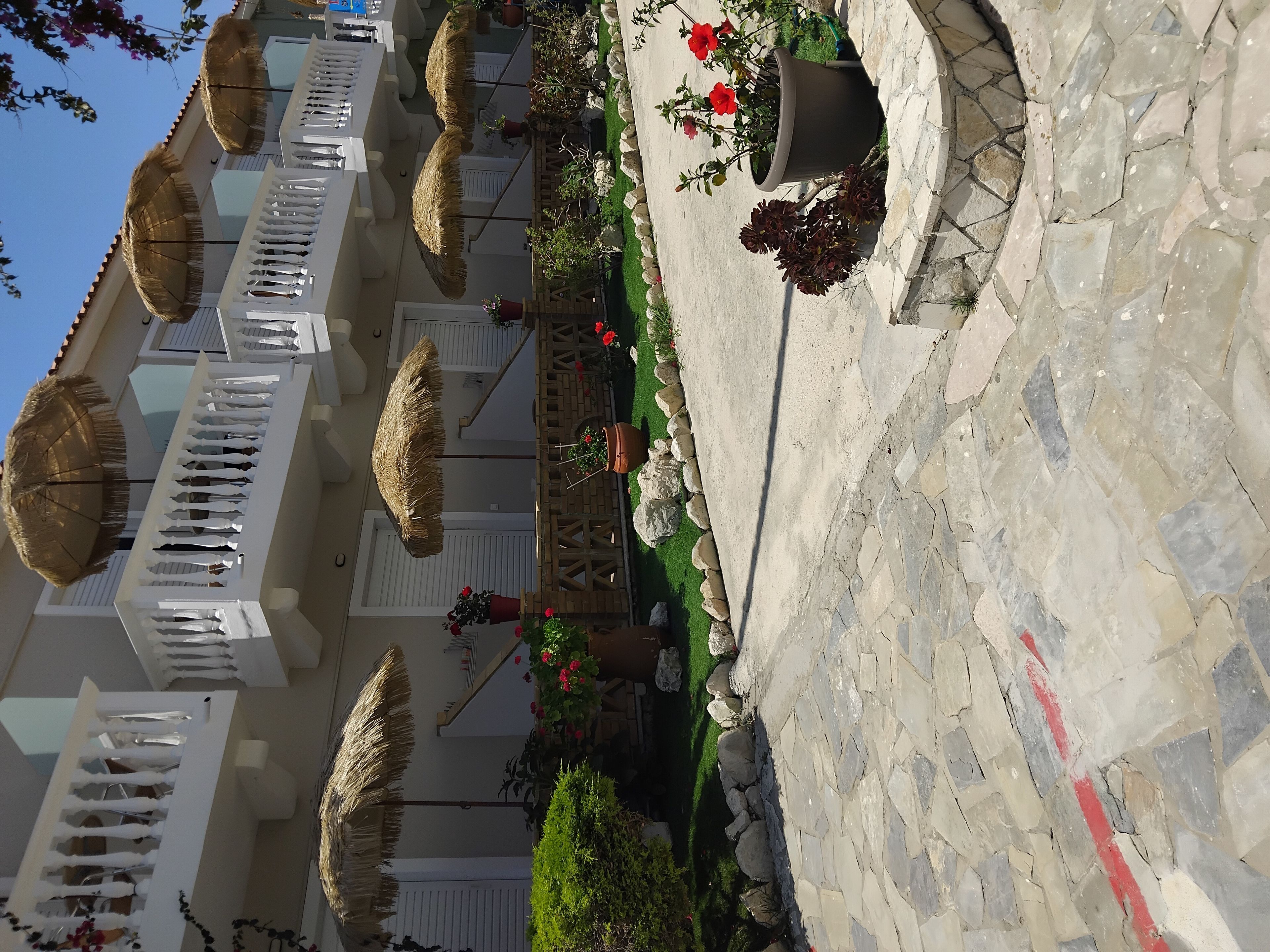 A hotel courtyard with thatched umbrellas, potted plants, and a stone wall.
