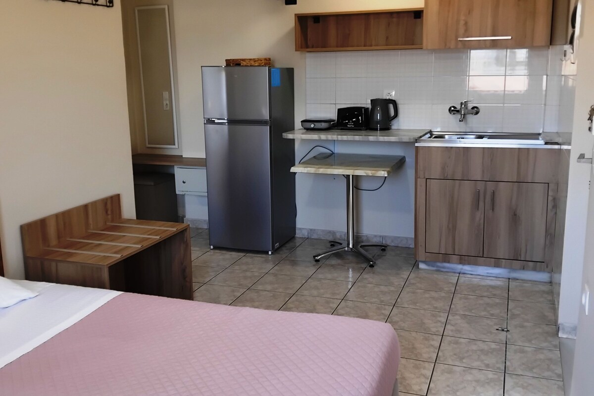 Quarto compacto com cama, cozinha compacta, pequena mesa de jantar e televisão fixada na parede.