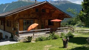 Un chalet en bois doté d’un balcon, d’un parasol rouge et surplombant un paysage montagneux.