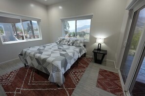Un dormitorio con cama, dos ventanas, una mesita de noche y vistas a la montaña.
