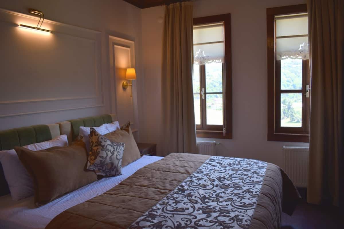 Ein Schlafzimmer mit einem Bett, einer Wandlampe und zwei mit Vorhängen versehenen Fenstern.