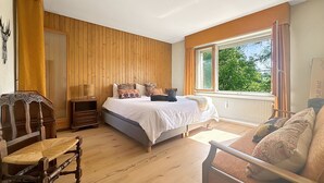 Un dormitorio con una cama grande, paredes de madera, una ventana con cortinas, una silla y una mesita de noche.