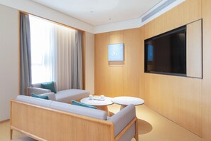 Ein modernes Hotelzimmer mit einer Sitzecke, einem kleinen runden Tisch, einem flachbildfernseher an der Wand und einem großen Fenster mit Vorhängen.