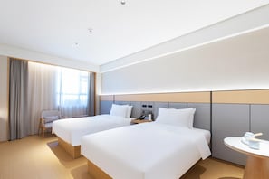 Ein Hotelzimmer mit zwei Betten, einem Schreibtisch, einem Stuhl, einem kleinen Tisch und einem Fenster mit Vorhängen.