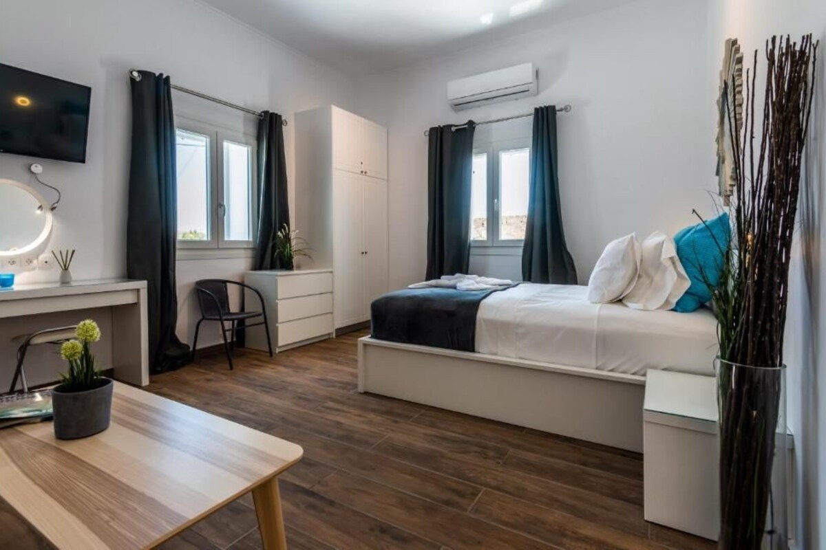 Quarto com cama, escrivaninha, cadeira, televisão e janela.
