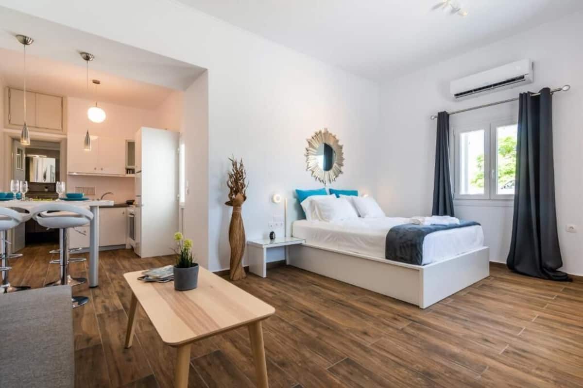 Une pièce de taille modeste comprenant un lit, une petite table, un coin cuisine et une fenêtre avec des rideaux.
