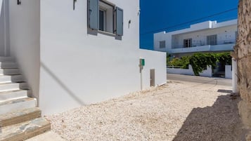 Um edifício branco com uma escadaria que leva a uma porta, uma janela com persianas e um caminho de acesso de cascalho.