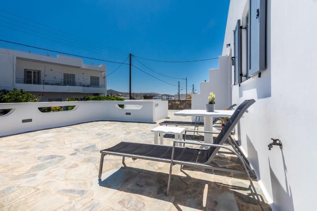 Um terraço no topo do edifício com piso de pedra, paredes brancas e uma pequena mesa com uma cadeira.