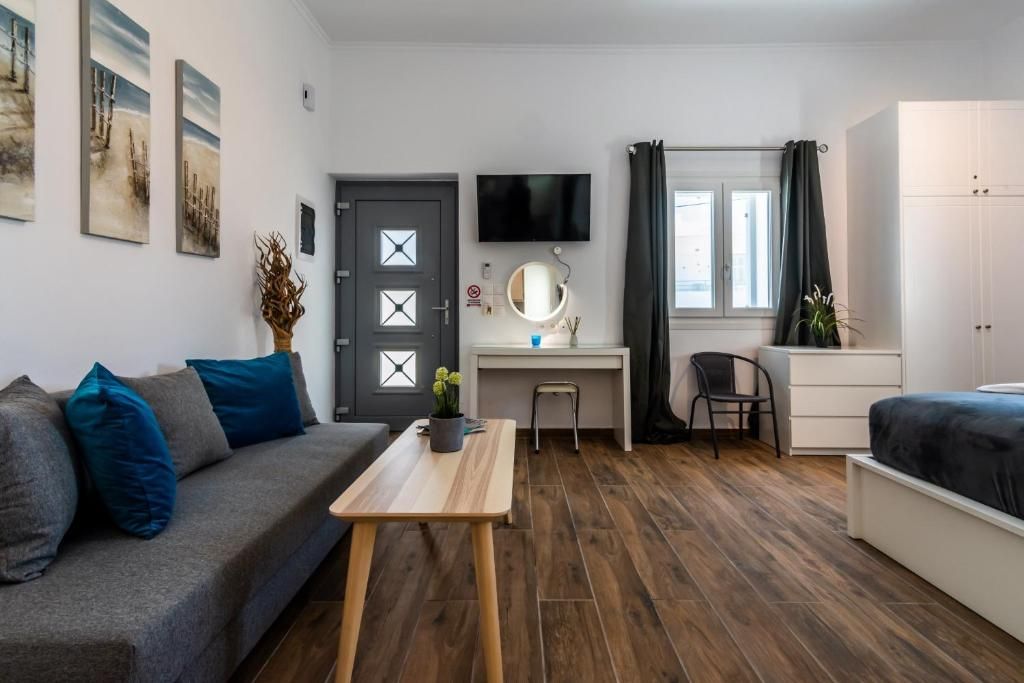 Quarto compacto com sofá, escrivaninha, cama, televisão e janela com cortinas.