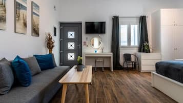 Quarto compacto com sofá, escrivaninha, cama, televisão e janela com cortinas.