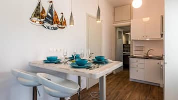 Cozinha moderna com armários brancos, bancada de mármore e área de jantar com mesa branca e cadeiras azuis.