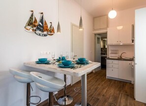 Cozinha moderna com armários brancos, bancada de mármore e área de jantar com mesa branca e cadeiras azuis.