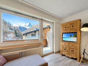 A room with a large window offering a mountain view, a wooden cabinet with a television, and a radiator. - Eagle Apartement - Zermatt by Interhome (Zermatt)