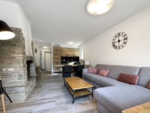A modern living room with a stone fireplace, a grey sofa, a wooden coffee table, and a kitchen in the background. - Eagle Apartement - Zermatt by Interhome (Zermatt)
