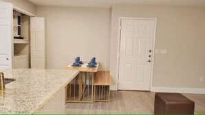 A kitchen with a granite countertop, a wooden dining table with blue chairs, a white door, and a brown bench. - Rust King 2Bed 2Bath / By TMC /5 min walk to NRG (Houston)