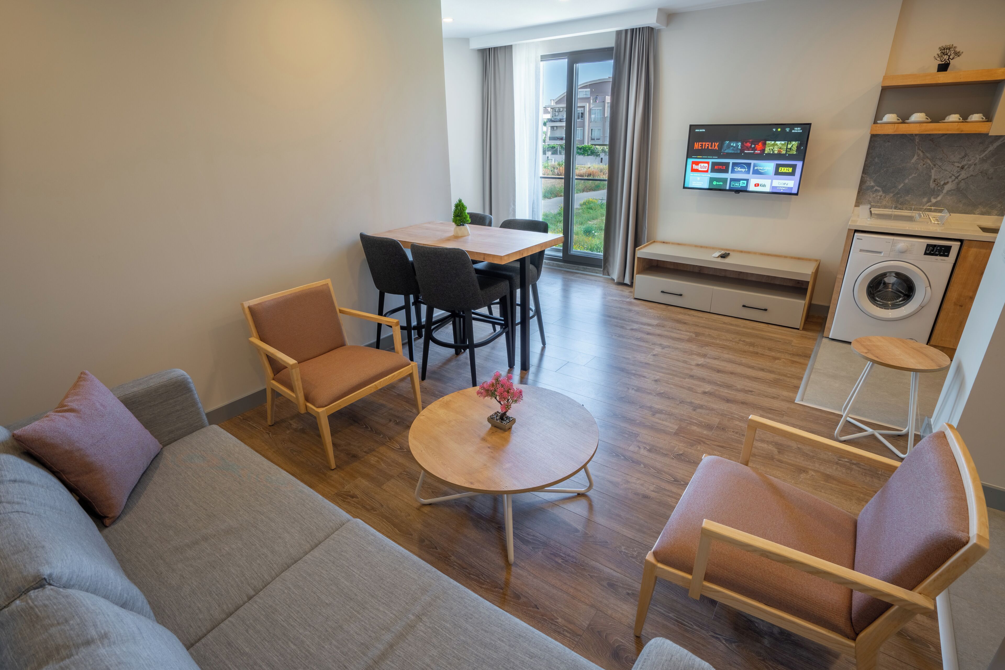 A modern living room with a sofa, chairs, a round table, and a TV mounted on the wall.