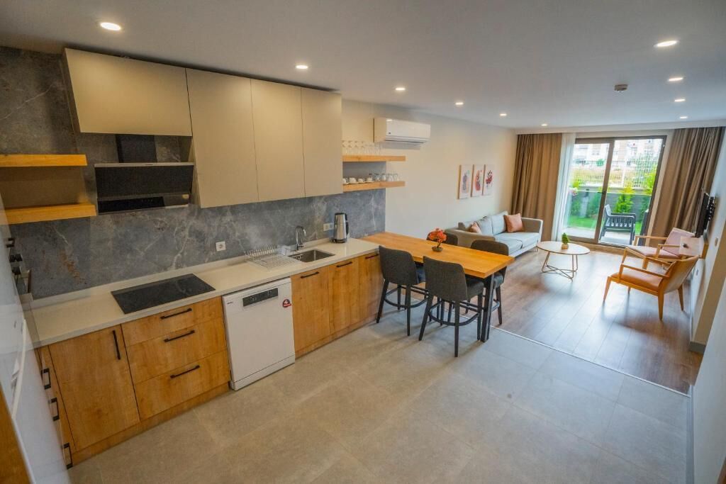 A modern kitchen with wooden cabinets, a dining area with a table and chairs, and a view of a garden through a sliding door.