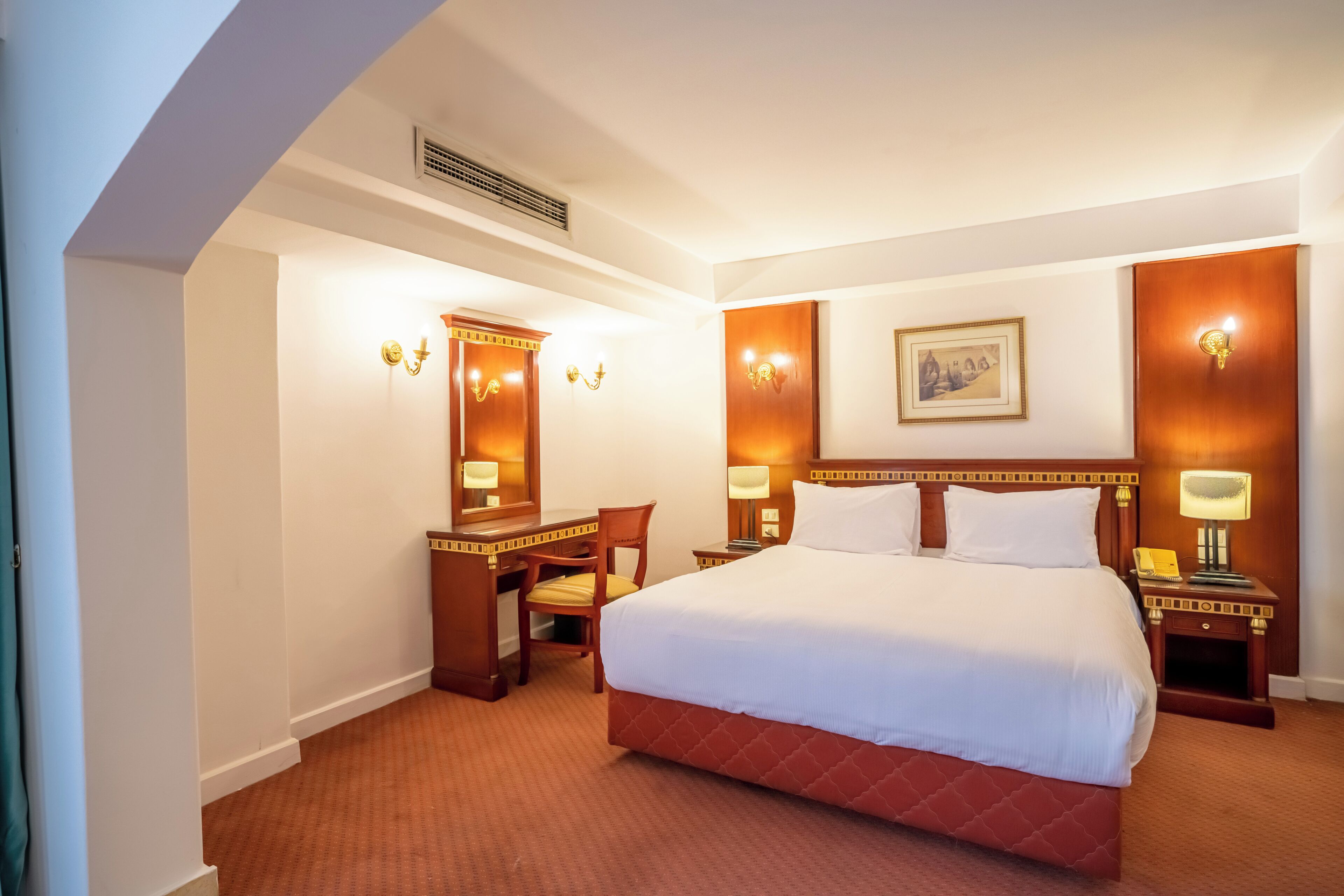 A hotel room with a large bed, a desk, a chair, and a desk lamp.