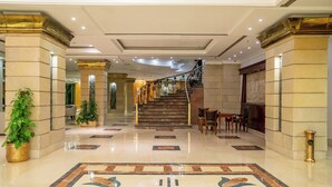A spacious lobby with a marble floor, a staircase, and a reception desk.