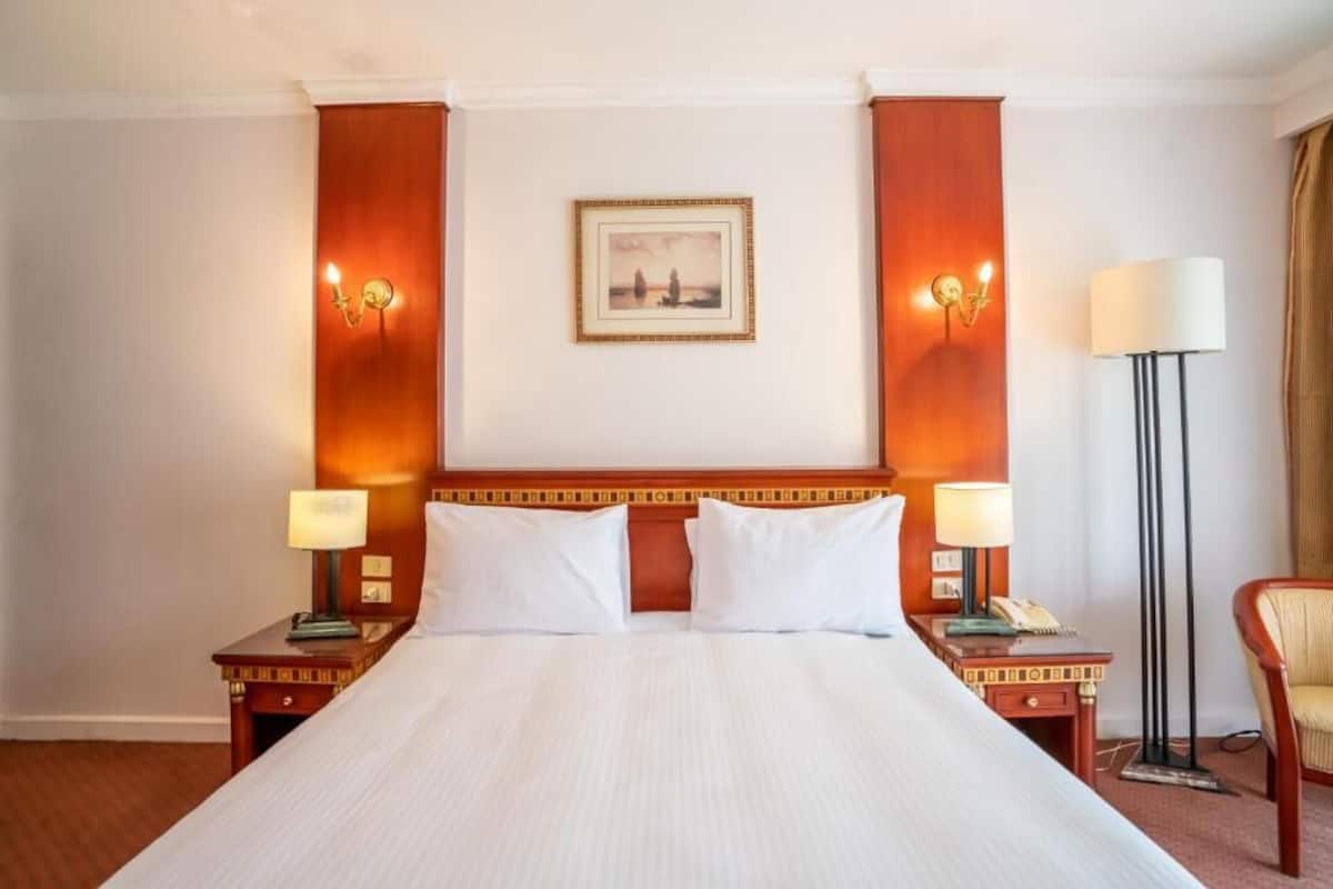 A hotel room with a large bed, two bedside tables with lamps, a framed picture on the wall, and a floor lamp.