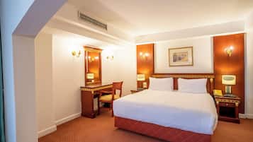 A hotel room with a large bed, a desk, a chair, and a desk lamp.