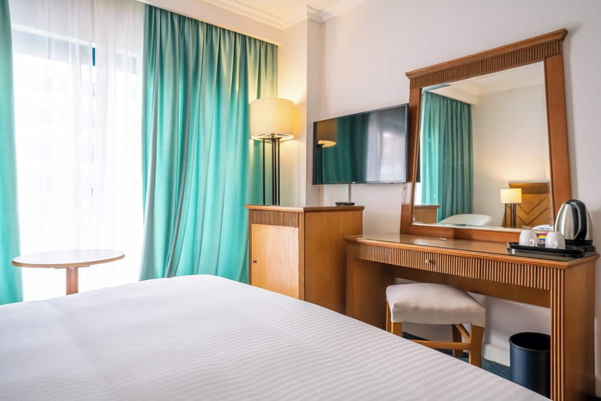 A hotel room with a bed, a desk with a chair, a TV, and a mirror.