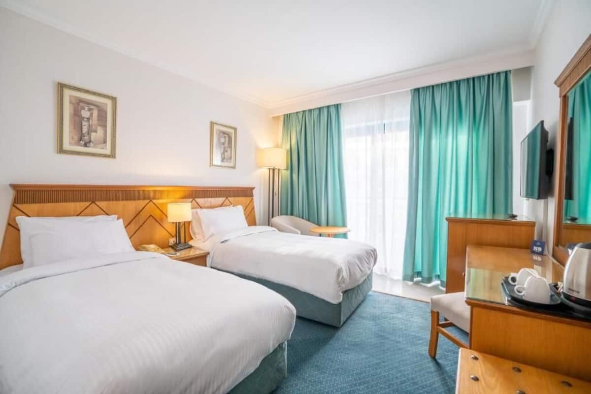 A hotel room with two beds, a desk, a chair, a coffee maker, and a television.