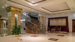A lobby with a marble floor, a staircase with ornate railings, and a large mural on the wall.