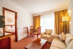 Una habitación de hotel con cama, sofá, mesa de comedor con sillas, televisor y lámpara.