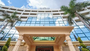 A modern hotel with a glass facade, palm trees, and a classical entrance.