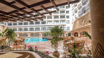 Un vestíbulo de hotel con piscina, zona de estar al aire libre y varios balcones.