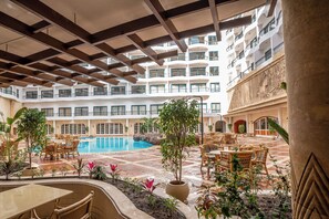 A hotel atrium with a pool, outdoor seating, and multiple balconies. - Azal Pyramids Hotel (Kafr ad-Dawwar)